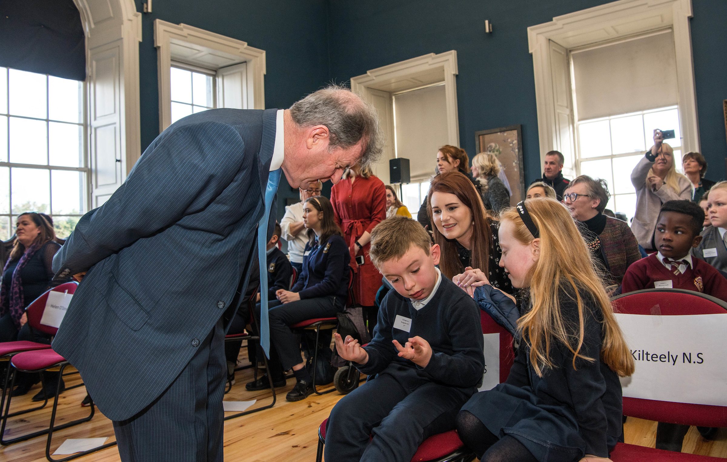 07/03/2019Eli O'Sullvian, 1st class, from Bulgaden NS, works out a maths question put to him by JP McManus, alongside senior infant student Carla O'Brien, and teacher Charlotte Reidy at the 'Design a TLC Bottle' prizegiving at the Hunt Museum, Limerick. Over 50 primary schools across the county entered ahead of Team Limerick Clean-Up 5, which will see thousands of volunteers take to the streets of Limerick city and county for Europe's largest one-day clean up. Sponsored by the JP McManus Benevolent Fund, the event has seen over 360 tonnes of litter gathered from the streets since inception in 2015. Over 14,000 volunteers have already signed up for the 2019 event, taking place on Good Friday, 19th April. Photo by Diarmuid Greene
